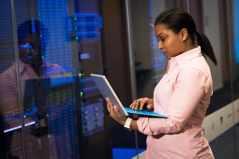 Professional woman analyzing data on a laptop in a server room, representing SaaS marketing funnel optimization and digital infrastructure management